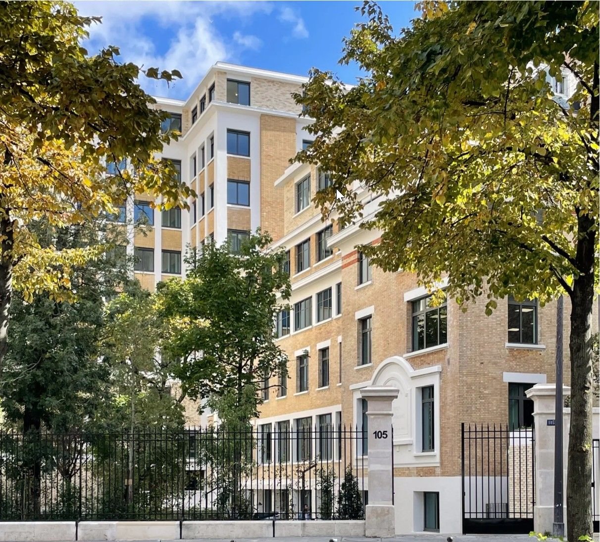Campus Raspail, bâtiment en brique et pierre derrière les grilles du boulevard Raspail